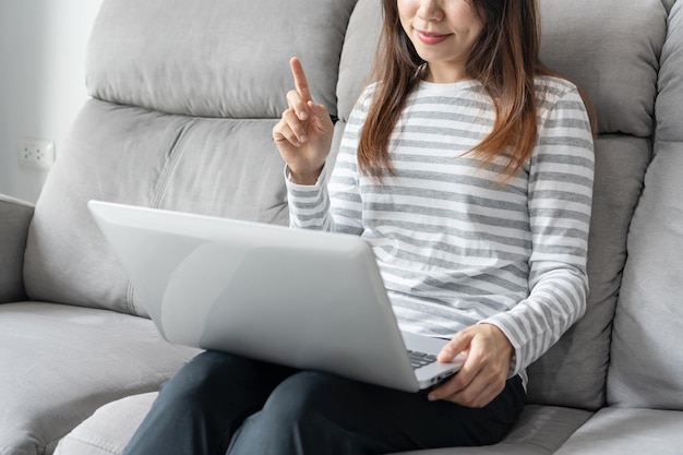 Asian woman using computer and communicates with family on the internet Girl sitting on sofa at home and video call with friend during Covid19 pandemic Technology and lifestyle new normal concept