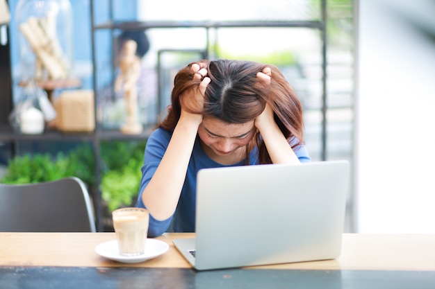 La donna asiatica che per mezzo del computer portatile del computer e beve il lavoro del caffè dal concetto domestico