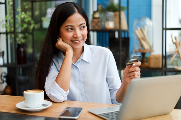 Asian woman using credit card shopping online in coffee shop cafe