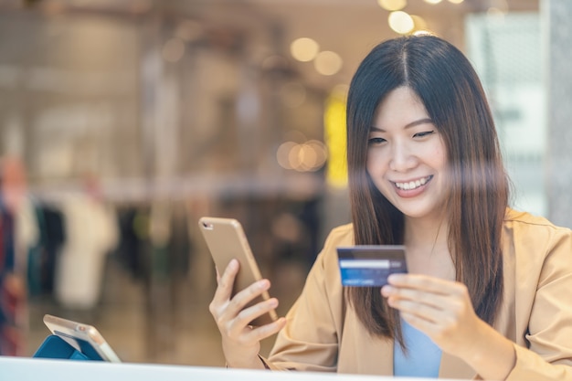 Asian woman using credit card with mobile phone for online shopping in department store