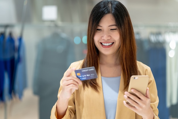 Asian woman using credit card with smart mobile phone for online shopping in department store