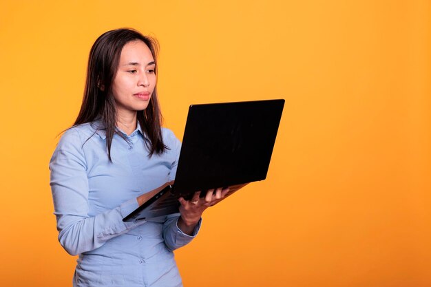 Азиатская женщина с помощью цифрового устройства просматривает веб-страницы в Интернете, ищет информацию для исследовательского проекта. Молодой взрослый использует портативный компьютер для навигации в социальных сетях. Концепция удаленной работы