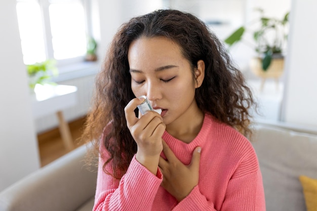 Asian woman using inhaler while suffering from asthma at home Young woman using asthma inhaler Closeup of a young Asian woman using asthma inhaler at home