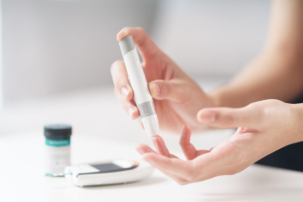 Photo asian woman using lancet on finger for checking blood sugar level by glucose meter healthcare and medical diabetes glycemia concept