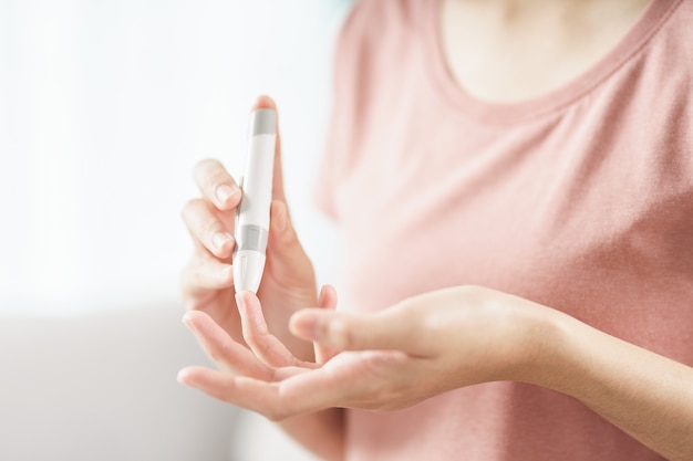 Asian woman using lancet on finger for checking blood sugar level by Glucose meter, Healthcare and Medical, diabetes, glycemia concept