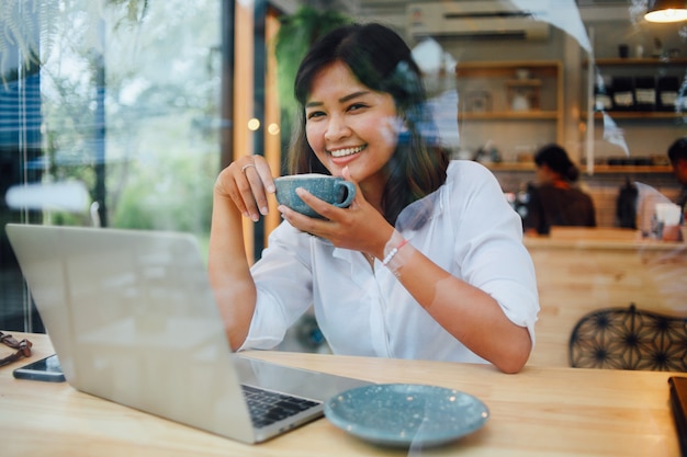 アジアの女性がコーヒーショップカフェでラップトップコンピューターを使用して