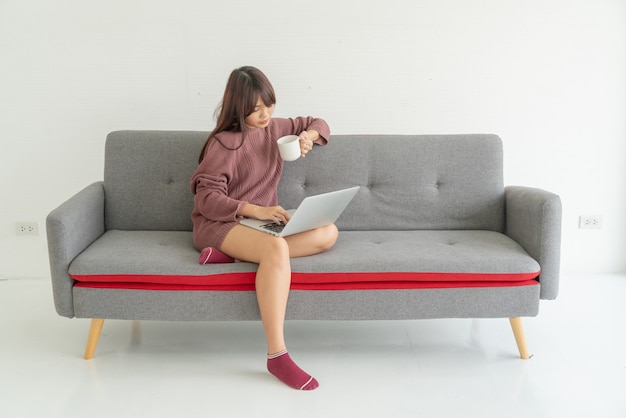 Asian woman using laptop on sofa in living room
