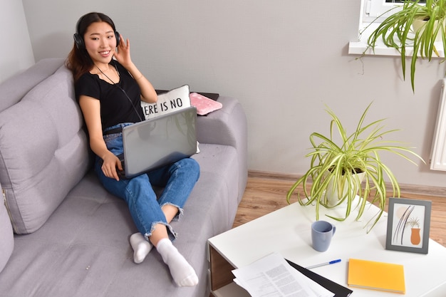 Donna asiatica che per mezzo del computer portatile sul sofà