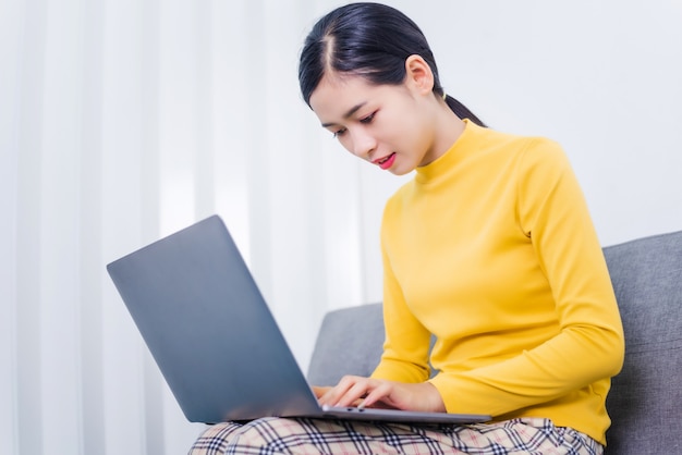 Asian woman using a laptop while sitting on a sofa