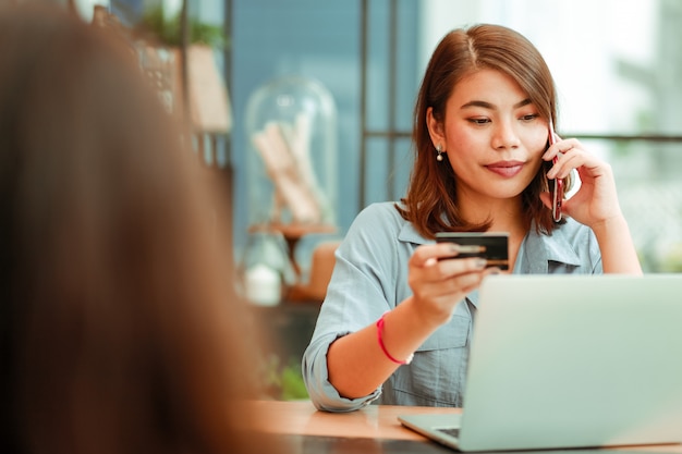 Asian woman using mobile phone with credit card and laptop computer for shopping online payment in coffee shop