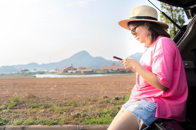 모바일 스마트폰에서 내비게이션이나 GPS를 사용하는 아시아 여성 그녀는 여행할 곳을 찾고 있는 차 뒤에 앉아 있었다