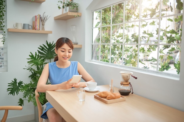 Asian woman using phone while having breakfast