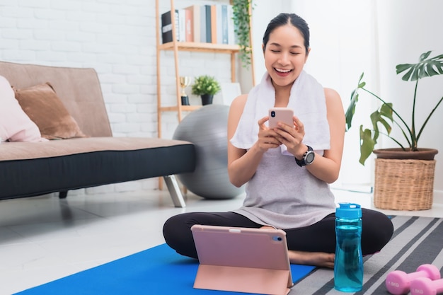 Donna asiatica che utilizza smartphone dopo aver giocato a yoga