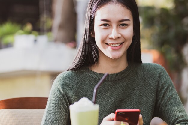 アジアの女性がスマートフォンを使用して、飲み物を飲みながらリラックスして楽しく、幸せ