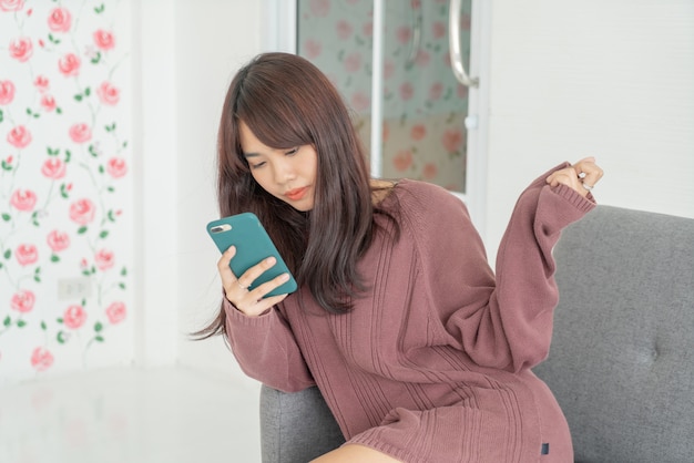 Asian woman using smartphone on grey sofa in living room