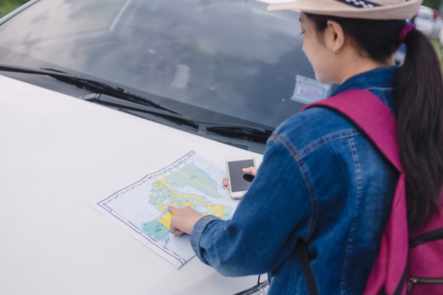 Asian woman using smartphone and map between driving car on road trip