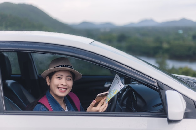 Asian woman using smartphone and map between driving car on road trip