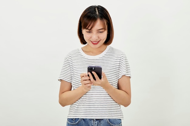 白い背景に携帯電話でのテキストメッセージに対して立っているスマートフォンを使用しているアジアの女性