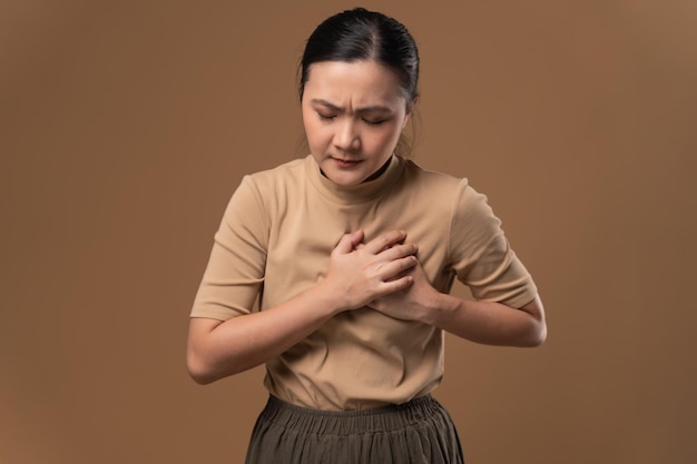 Asian woman was sick with chest pain standing isolated on beige background