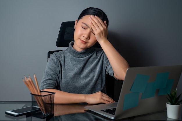 Asian woman was sick with headache, touching her head, working on a laptop at office 