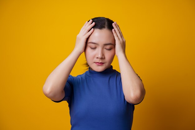 Asian woman was sick with headache touching her head on yellow.