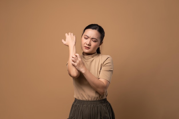 Asian woman was sick with irritate itching her skin scratching\
her skin standing isolated on beige background