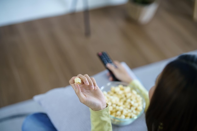 스마트 TV를 시청하고 리모콘을 사용하는 아시아 여성 리모콘 텔레비전으로 집에서 텔레비전 오디오 리모콘을 들고 있는 손