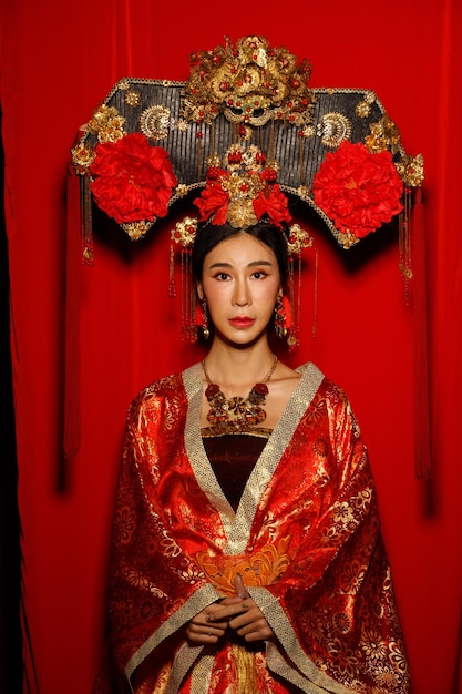 Asian woman wear china royal empress traditional costume with\
golden line design dress and headwear dramatic series female stand\
half body with fabric fluttering in the air tone red\
background