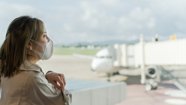 アジアの女性は空港ターミナルで旅行中にマスクを着用します。新しい正常なcovid19疾病予防の概念。