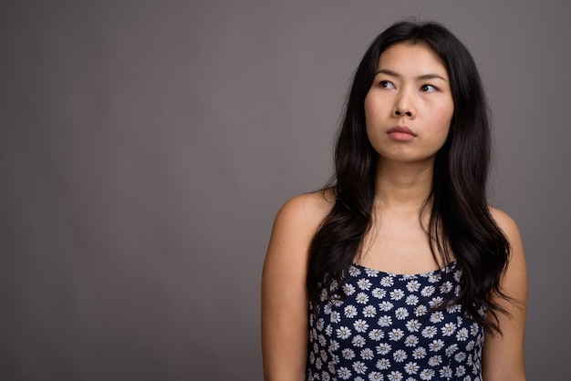 Asian woman wearing blue dress against gray wall