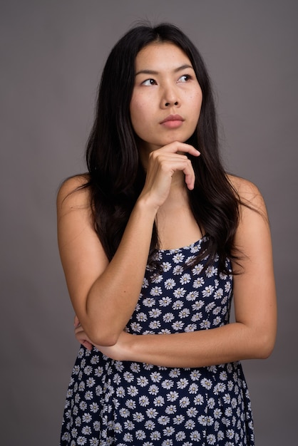 Asian woman wearing blue dress against gray wall