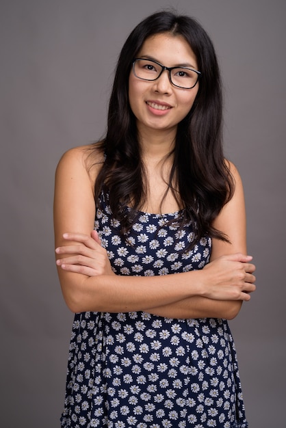 Asian woman wearing blue dress and eyeglasses against gray space