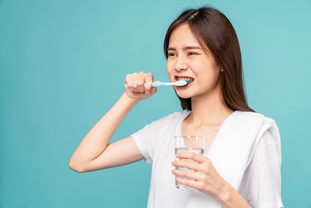 Asian woman wearing braces with brushing teeth and holding water glass, towel on the shoulder on blue background, Concept oral hygiene and health care.