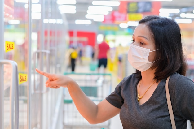 Asian woman wearing disposable medical mask shopping in supermarket during coronavirus epidemic