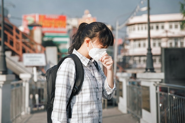 Maschera di protezione d'uso della donna asiatica che tossisce a causa di inquinamento atmosferico nella città