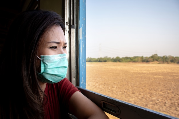 Foto maschera di protezione d'uso della donna asiatica e guardare attraverso la finestra del treno