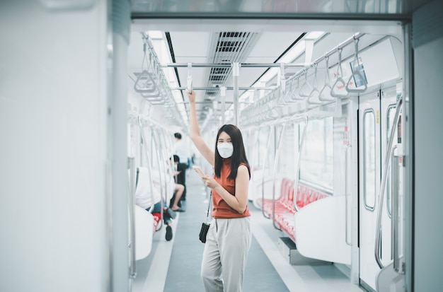 마스크를 쓰고 지하철에서 스마트폰을 사용하는 아시아 여성, 대중 교통 안전, 코비드-19 전염병 동안의 뉴 노멀