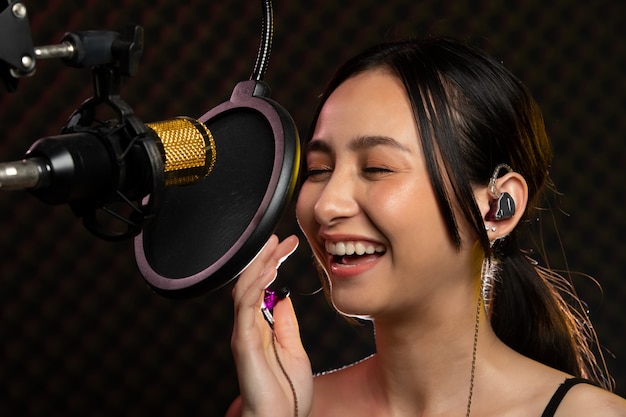 Asian Woman wearing headphones singing with a hanging microphone. SoundProof room.