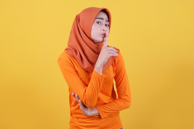 Asian woman wearing hijab worried, nervous, panicked, aggressive, angry woman demonstrates a gesture of silence, holding an index finger near the mouth