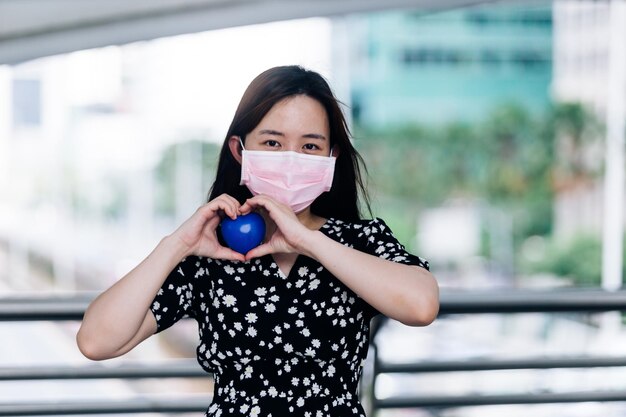 Asian woman wearing mask and holding a blue heart in the city