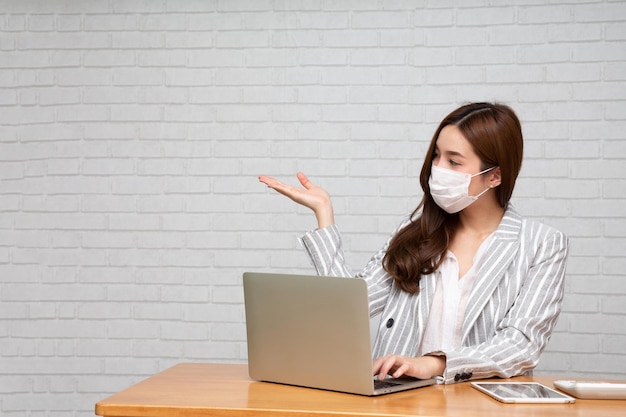 Asian woman wearing mask and presenting  with copy space and sitting with computer laptop at home