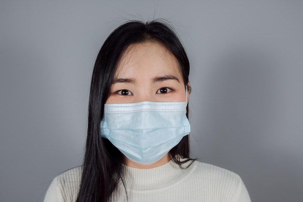 Asian woman wearing a medical face mask to protect Covid19 Coronavirus on gray background