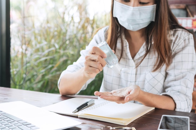 Donna asiatica che indossa una maschera medica e applica gel disinfettante per le mani sulla mano durante la crisi del coronavirus misure protettive per prevenire il concetto di trasmissione covid19 primo piano