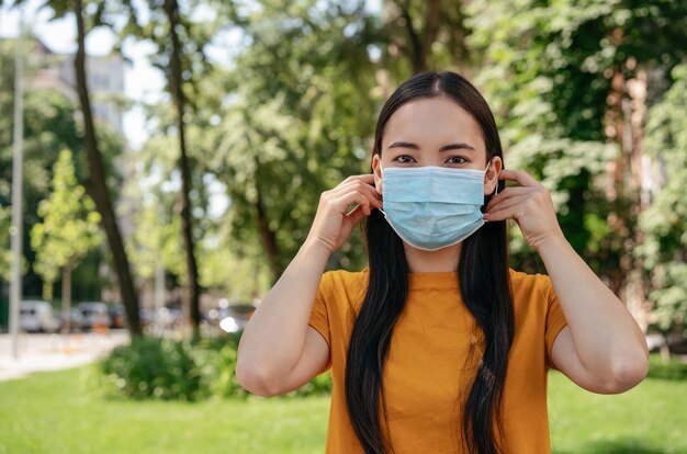 Photo asian woman wearing medical mask looking at camera outdoors