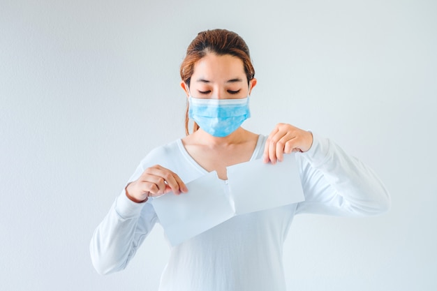 La donna asiatica che indossa la maschera medica strappa un libro bianco in bianco