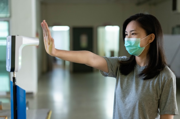 An Asian woman wearing an oil mask stands to check the day's body temperature