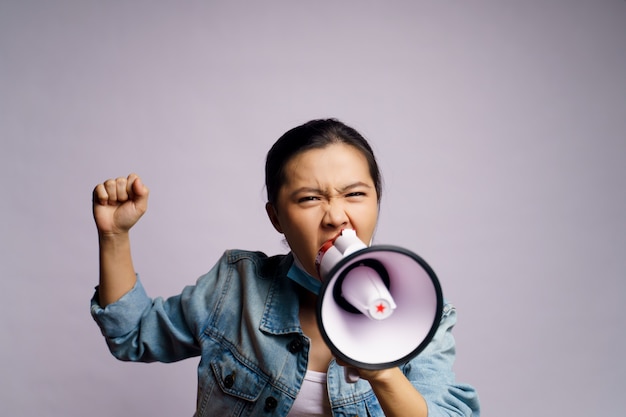 Asian woman wearing protective face mask shouting with megaphone isolated.