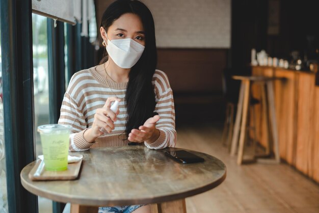 Asian woman wearing protective mask using alcohol antiseptic gel prevent outbreak of Covid19 in cafe