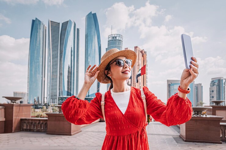 Photo asian woman wearing red dress and straw hat taking a selfie with smartphone in front of skyscrapers in abu dhabi