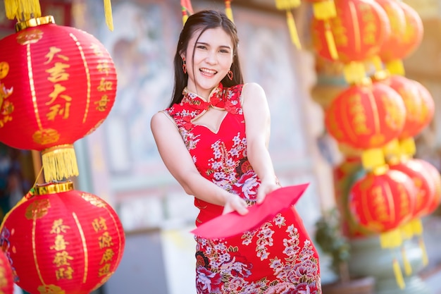 赤い封筒を手に持って、赤い伝統的な中国のチャイナドレスを着ているアジアの女性